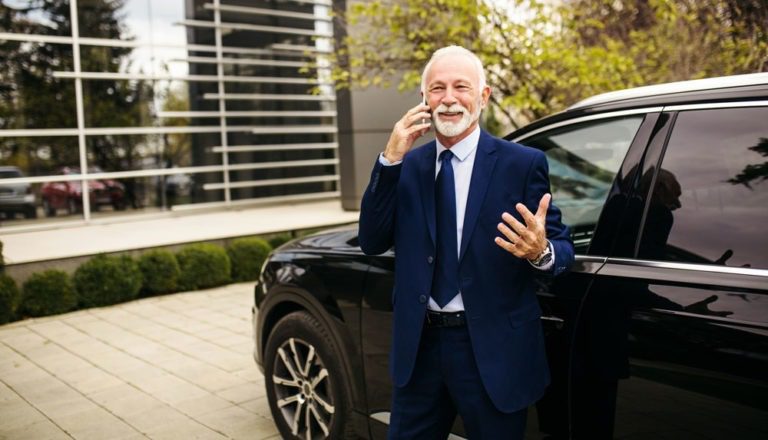 Businessman in a suit and tie talking on the phone next to a parked car.