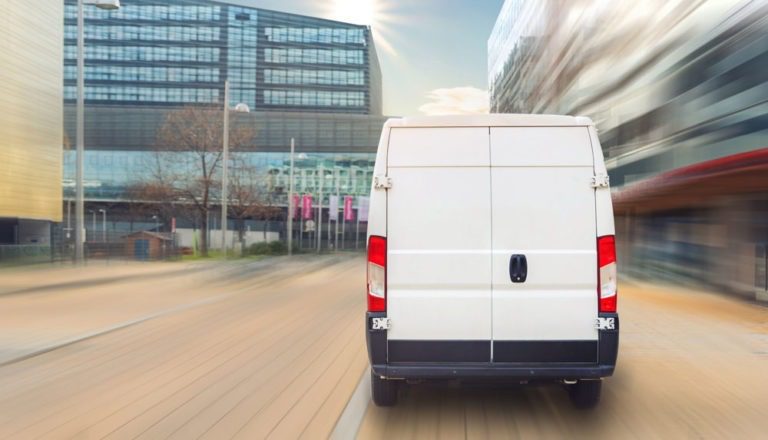 White service or delivery van driving in a downtown area with a blurred background.