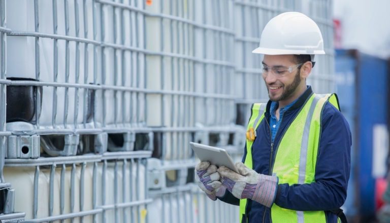 Engineer in a vest and hard hat looking at a tablet at a worksite.