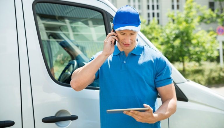 Worker on the phone and looking at a digital tablet ouside of his white mobile workforce van.