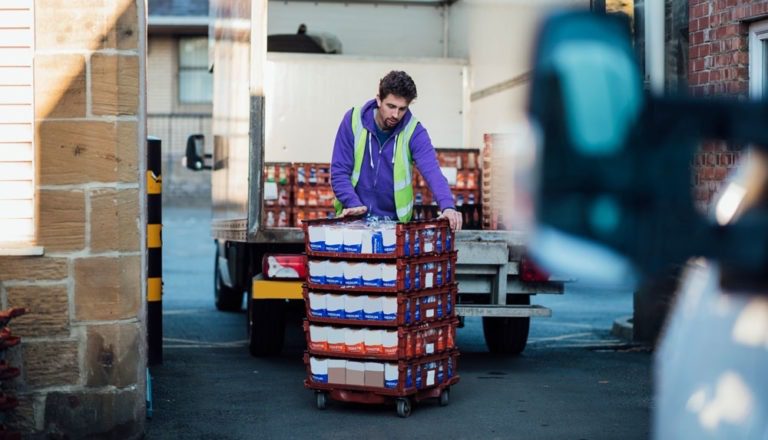 Worker wearing a safety vest and pushing a pallet of bread after unloading it from a delivery truck.